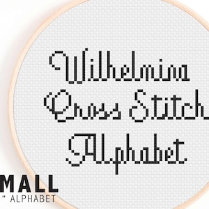 May include: A white embroidery hoop with black cross stitch lettering that reads "Wilhelmina Cross Stitch Alphabet".