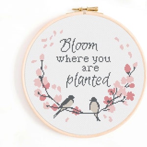 May include: Cross stitch embroidery hoop with a floral design and two birds. The text reads "Bloom where you are planted."