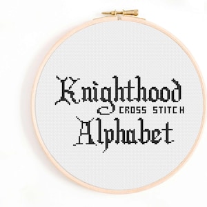 Pode incluir: Um aro de bordado branco com letras de ponto cruz pretas que dizem "Knighthood Cross Stitch Alphabet".