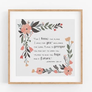 May include: Framed print featuring a cross-stitch design with floral accents in peach, pink, and green. The text reads "For I know the plans I have for you..." from Jeremiah 29:11. The artwork is in a light wood frame.