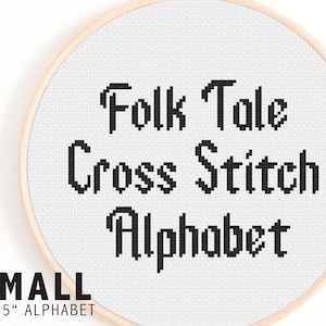 May include: A white embroidery hoop with black text that reads "Folk Tale Cross Stitch Alphabet" in a stylized font. The hoop is 1-1.5 inches in diameter.