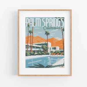 Pode incluir: Uma impressão emoldurada com uma ilustração pixelizada de Palm Springs, Califórnia. A obra de arte retrata uma piscina, palmeiras e montanhas em tons de azul, laranja e verde. As palavras "PALM SPRINGS" e "California" são exibidas no topo.