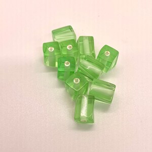 May include: A group of light green glass beads with a square shape and a hole in the center. The beads are translucent and have a slight shimmer.
