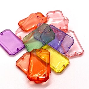 May include: Assortment of colorful, faceted, rectangular plastic charms with a hole in the center. The charms are in shades of purple, green, yellow, orange, and pink.