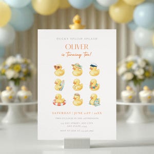 May include: A white birthday invitation card featuring the text DUCKY SPLISH SPLASH, OLIVER is Turning Two!, and event details. The design includes nine watercolour illustrations of yellow rubber ducks with various accessories like hats and floats.