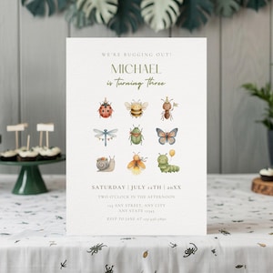 Puede incluir: Una invitación de cumpleaños color crema con el texto "We're bugging out!" y "Michael is turning three." Presenta ilustraciones de acuarela de varios insectos. También se incluye la fecha y la hora.