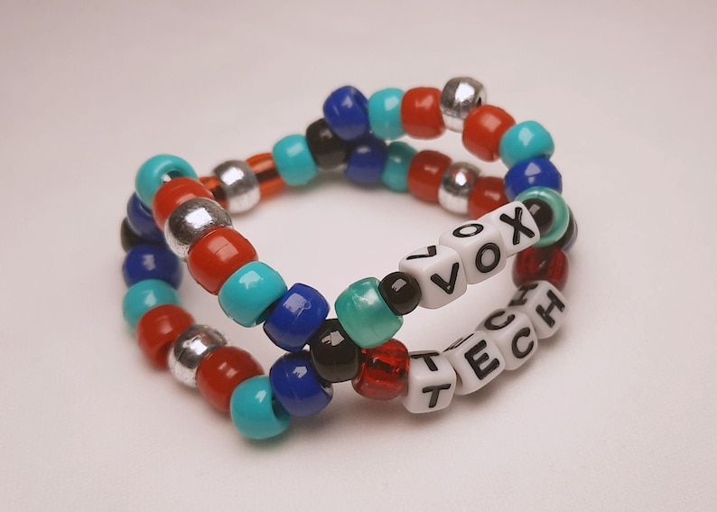 Peut inclure: Deux bracelets de perles. L'un porte le mot "VOX" et l'autre "TECH" en perles blanches. Les bracelets sont faits de perles color&eacute;es rouges, bleues, turquoise, argent&eacute;es et noires.