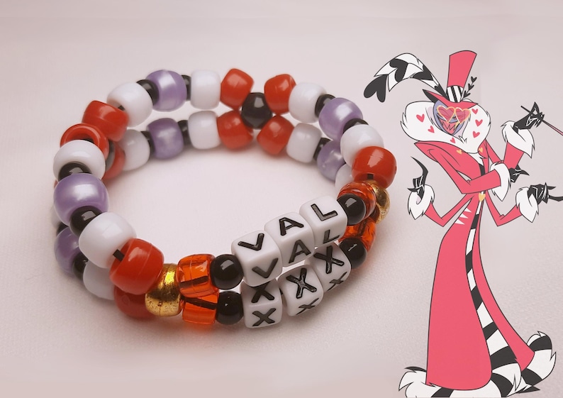 Peut inclure: Un bracelet de perles &agrave; deux rangs avec le mot "VAL XXX" &eacute;crit en perles blanches. Le bracelet est compos&eacute; de perles rouges, oranges, noires, blanches, violettes et dor&eacute;es. Un personnage de dessin anim&eacute; en rouge et noir est en arri&egrave;re-plan.