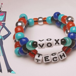 Peut inclure: Un bracelet de perles color&eacute;es avec les mots "VOX TECH" &eacute;pel&eacute;s en perles blanches. Le bracelet pr&eacute;sente des perles rouges, bleues, turquoise, noires et argent&eacute;es. Une illustration d'un personnage de dessin anim&eacute; avec une t&ecirc;te de t&eacute;l&eacute;vision est &agrave; gauche.