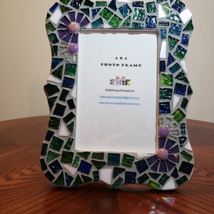 Puede incluir: Un marco de fotos de 4x6 hecho de mosaicos en tonos verdes, azules y morados. El marco tiene un borde decorativo con un dise&ntilde;o floral. El marco est&aacute; hecho por KatMosaicKreations e incluye su informaci&oacute;n de contacto.
