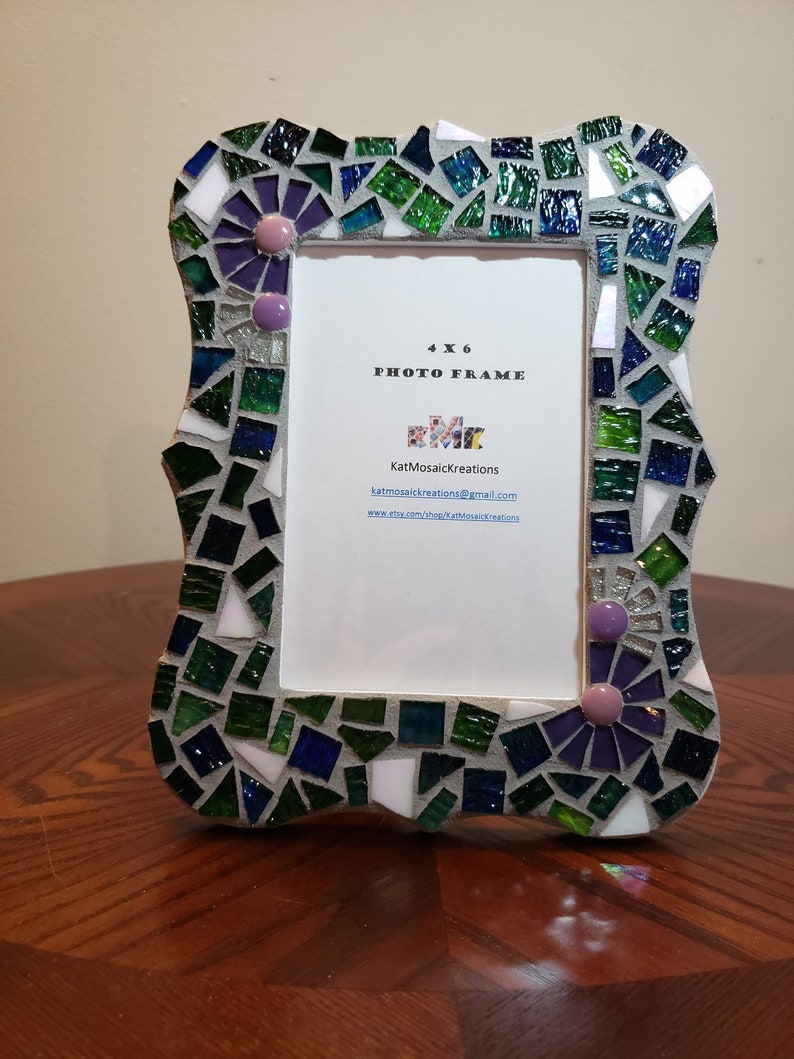 Puede incluir: Un marco de fotos de 4x6 hecho de mosaicos en tonos verdes, azules y morados. El marco tiene un borde decorativo con un dise&ntilde;o floral. El marco est&aacute; hecho por KatMosaicKreations e incluye su informaci&oacute;n de contacto.