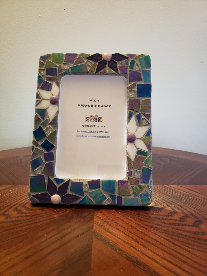 Puede incluir: Un marco de fotos de mosaico de 4x6 con un dise&ntilde;o de mosaico azul, verde y morado. El marco tiene flores blancas con centros rosados alrededor de los bordes. El marco tiene el texto "4x6 Photo Frame" y "KatMosaicKreations" en &eacute;l.