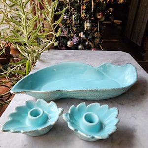 May include: A turquoise ceramic serving dish and two leaf-shaped candle holders with gold trim. The serving dish is oblong with a textured surface. The candle holders have a central well for candles.