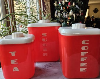 Könnte beinhalten: Drei rote Plastikbehälter mit weißen Deckeln und weißen Beschriftungen. Die Behälter sind mit "TEA", "SUGAR" und "COFFEE" beschriftet.