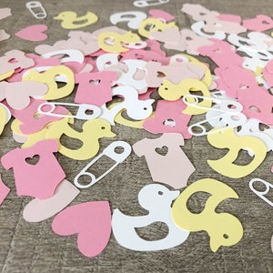 May include: Pink, yellow, and white paper confetti with baby shower themes. The confetti includes baby onesies, ducks, hearts, and safety pins.