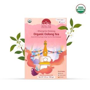 Könnte beinhalten: Eine rosa und weiße Schachtel mit USDA Organic Shangrila Oolong Organic Oolong Tea von Nepal Tea Collective. Die Schachtel zeigt eine Illustration eines Stupas mit Gebetsfahnen und einer Bergkette. Der Text auf der Schachtel lautet "Award Winning Single Origin Tea from the Himalayas". Die Schachtel enthält auch eine Liste von Geschmacksnoten: Kekse, süße Gewürze und Karamell. Das Nettogewicht des Tees beträgt 3,5 oz oder 100 g.
