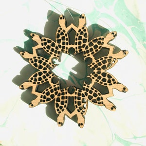 Può includere: Ornamento in legno con un design circolare di tartarughe interconnesse. Ogni tartaruga ha un guscio a motivi, creando un pezzo decorativo a tema natura. L'ornamento è realizzato in legno di colore chiaro.