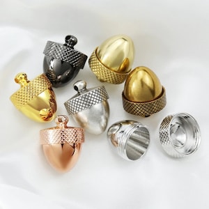 May include: Assortment of eight acorn-shaped metal containers in various finishes, including gold, silver, copper, and black. The containers have a textured, ridged design and are open at the top.