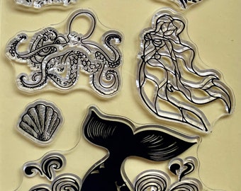 May include: A set of clear rubber stamps featuring a mermaid, an octopus, a whale tail, a seashell, and a wave pattern. The stamps are designed for crafting and scrapbooking.