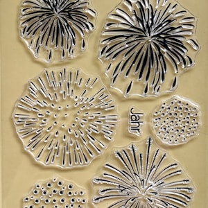 Puede incluir: Juego de sellos transparentes con diseños de fuegos artificiales en blanco y negro. Incluye el texto alemán "Glückliches neues" y la palabra "Jahr". Ideal para scrapbooking y creación de tarjetas.