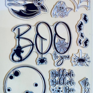 Könnte beinhalten: Ein Set mit transparenten Halloween-Stempeln mit Fledermäusen, Spinnen, Geistern, einem Mond und den Worten "BOO! to you" und "Bibbidi Bobbidi Boo".