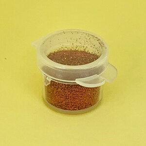 以下が含まれることがあります： 銅色のグリッターが詰まった小さな透明なプラスチック製の瓶