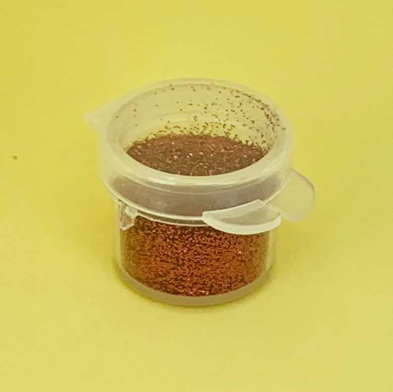 以下が含まれることがあります： 銅色のグリッターが詰まった小さな透明なプラスチック製の瓶