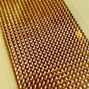 Può includere: Un foglio di strass adesivi color oro. Gli strass sono piccoli e di forma quadrata, disposti a griglia.