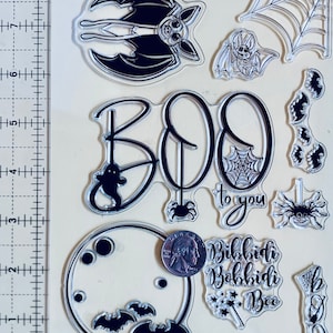 Könnte beinhalten: Ein Set durchsichtiger Halloween-Stempel mit Bildern von Fledermäusen, Spinnen, einem Mond, einem Spinnennetz und den Worten "BOO to you" und "Bibbidi Bobbidi Boo".