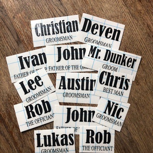 May include: A set of 11 white cards with black text, each card has a different name and title. The titles include "Groom", "Best Man", "Father of the Groom", "The Officiant", and "Groomsman".