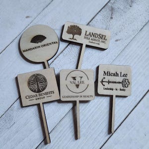 May include: A selection of wooden signs featuring company logos and text. The signs display phrases such as "Mandarin Oriental," "Landsel Title Agency, Inc.," "Cedar Benefits Group," "Val Lee Leadership in Realty," and "Micah Lee Leadership in Realty."