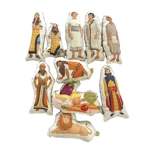 May include: Set of ten felt figures depicting characters from the Bible. The figures are colorful and detailed, with each character wearing traditional clothing. The set includes a lion, a basket of vegetables, and figures of men and women.