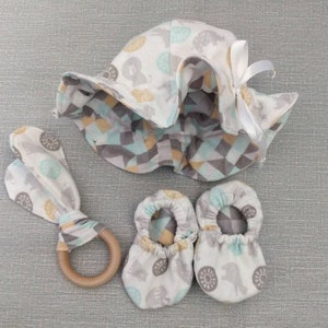 May include: A baby hat, booties, and a teether in a light blue, gray, and yellow geometric pattern. The hat has a white bow and the teether is made of wood.
