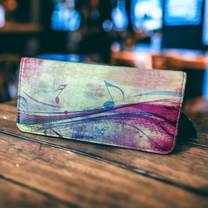 May include: A colourful leather wallet with a musical note design. The wallet has a light green background with purple, blue, and pink accents.