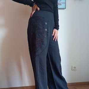 Puede incluir: Pantalón de pierna ancha, azul oscuro, con un parche decorativo en el lateral y varios botones. El pantalón tiene un corte holgado y un estilo informal.