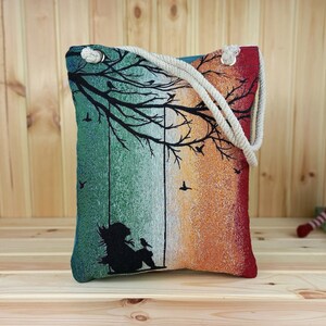eine bunte Frauen Schultertasche aus gewebtem 100% Baumwolle. Innen Baumwolle. Muster ist Silhouette einer Frau, die an einem Baum unter Vögel schaukelt. hell blaue Rückseite ist aus Samt.