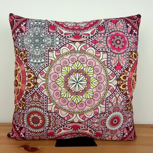 Puede incluir: Una almohada rosa y roja con un patrón de mandala. La almohada está hecha de tela y tiene una forma cuadrada.
