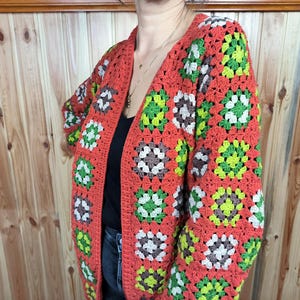 May include: A crocheted cardigan with a granny square pattern in shades of orange, green, and white.