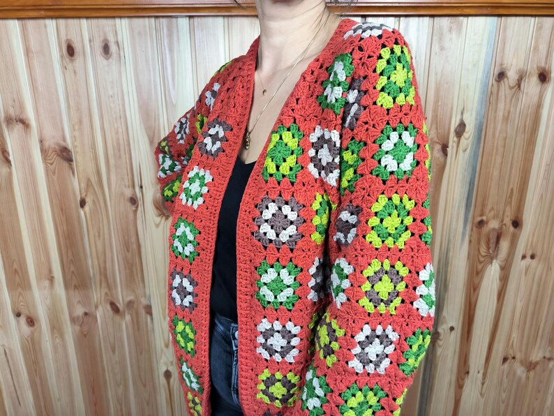 May include: A crocheted cardigan with a granny square pattern in shades of orange, green, and white.
