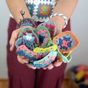 May include: A collection of colorful crocheted granny squares in various shades of blue, green, pink, and orange. The squares are held in a person's hands.