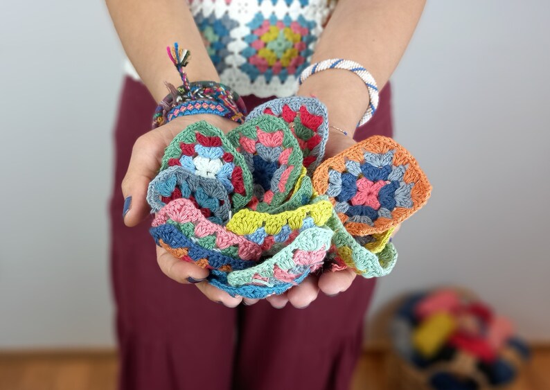 May include: A collection of colorful crocheted granny squares in various shades of blue, green, pink, and orange. The squares are held in a person's hands.