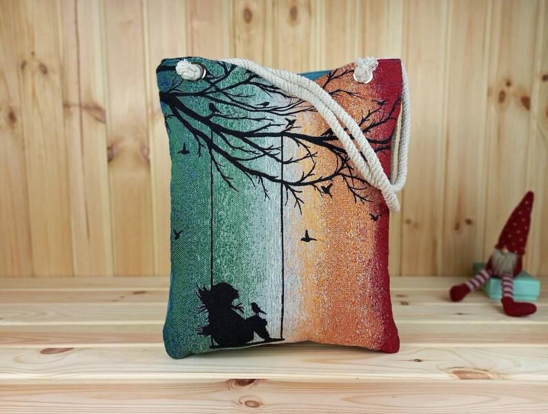 eine bunte Frauen Schultertasche aus gewebtem 100% Baumwolle. Innen Baumwolle. Muster ist Silhouette einer Frau, die an einem Baum unter Vögel schaukelt. hell blaue Rückseite ist aus Samt.