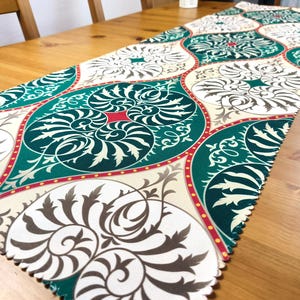 Pode incluir: Um corredor de mesa verde e branco com um padrão repetido de desenhos florais estilizados. O corredor de mesa tem uma borda vermelha e dourada.