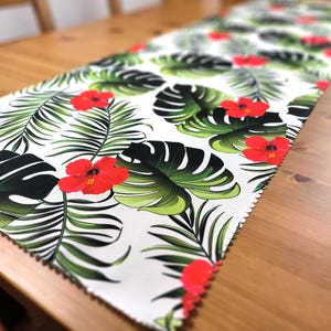 Peut inclure: Chemin de table blanc avec un imprimé tropical composé de feuilles vertes et de fleurs d'hibiscus rouges.