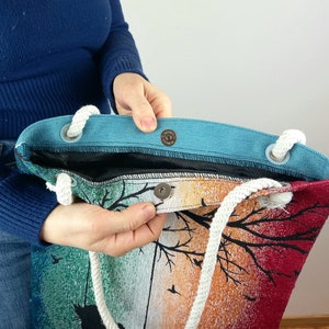 May include: A colorful tote bag with a sunset design and white rope handles. The bag has a blue lining and a snap closure.