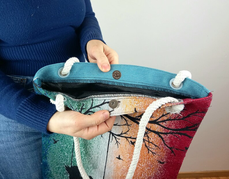 May include: A colorful tote bag with a sunset design and white rope handles. The bag has a blue lining and a snap closure.