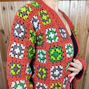 May include: A crocheted cardigan with a granny square pattern in shades of orange, brown, green, and white.