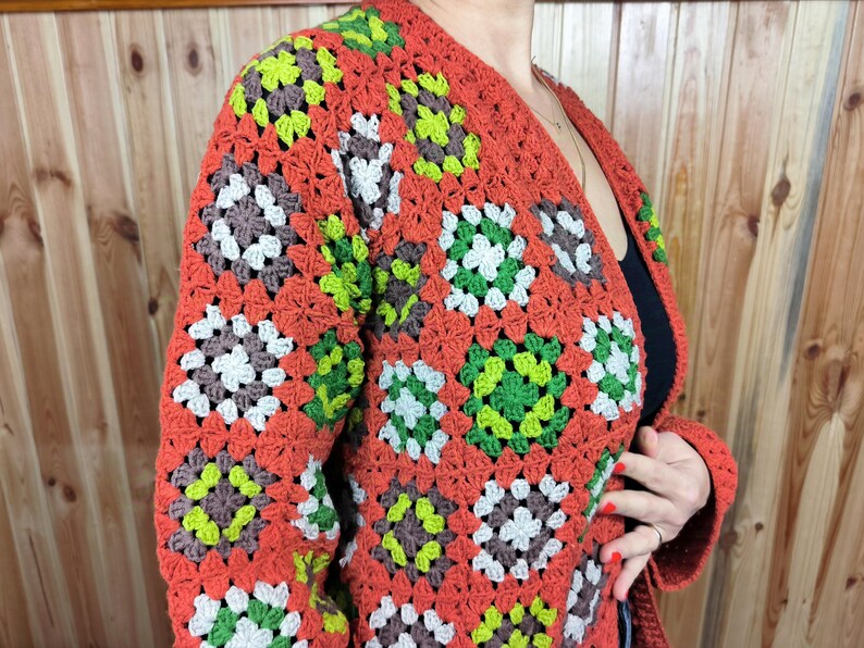 May include: A crocheted cardigan with a granny square pattern in shades of orange, brown, green, and white.
