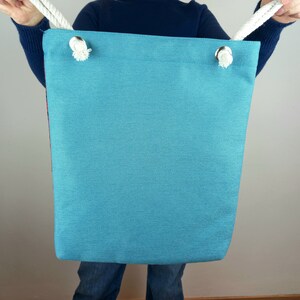 May include: A teal blue tote bag with white rope handles. The bag is made of a canvas material and has a simple design.