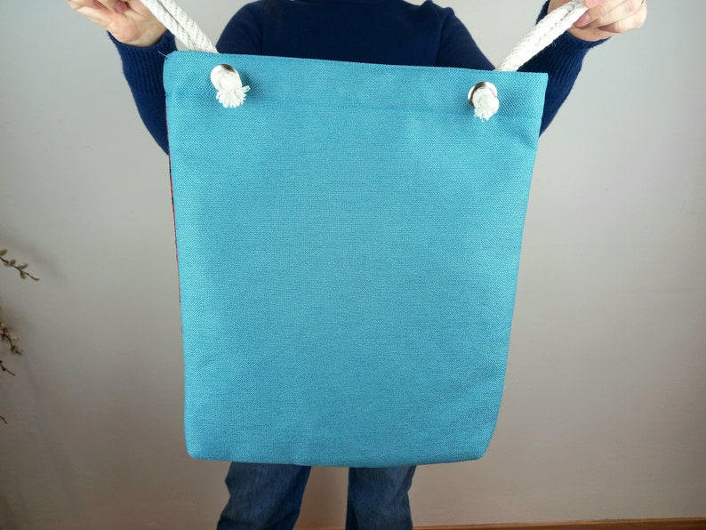 May include: A teal blue tote bag with white rope handles. The bag is made of a canvas material and has a simple design.